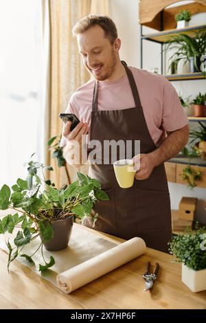 Man in apron holding cup, checking phone in small plant shop. Business owner multitasking during busy day. Stock Photo