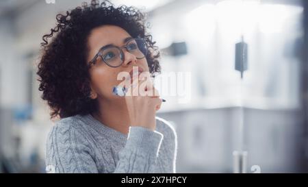 Young Black Female Genius Solves Complex Mathematical Problems and Writing Long Equations on the Whiteboard. Higher Education, Science, Technology and Innovation Concept. Stock Photo