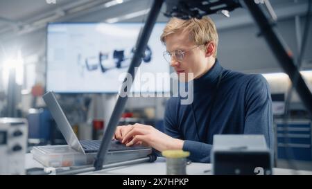 Young Caucasian Male Engineer Installs Processor in the Drone and Types on Laptop. Designing Unmanned Aerial Vehicle in Modern Laboratory. Breakthrough in Aviation Concept. Stock Photo
