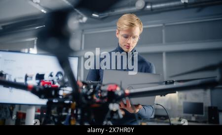 Young Male Developer Programming on Laptop Computer. Working on a New Modern Drone Design in the Research Center Laboratory. People Creating Futuristic Unmanned Aerial Vehicle Concept. Stock Photo