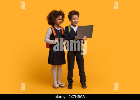 Two Smiling Schoolchildren With Backpacks Sharing a Laptop Stock Photo