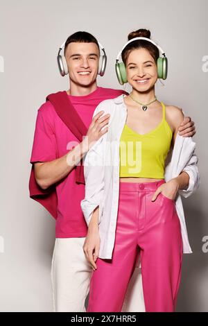 A stylish young couple, deeply in love, listening to music together wearing headphones against a sleek grey backdrop. Stock Photo