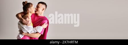 A stylish young man tenderly holds his partner in his arms against a grey studio backdrop. Stock Photo