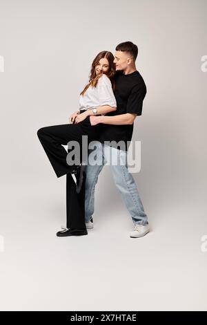 A man tenderly holds a woman in his arms, expressing love and affection in a studio setting with a grey background. Stock Photo