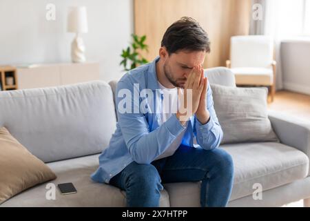 Young Man Sitting on Sofa With Hands Covering Face Stock Photo