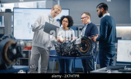 Diverse Group of Young Specialists Talk with Chief Engineer. Professionals use Laptop and Working on Electric Engine Design. Scientific Startup for Futuristic Sustainable Energy Solution. Stock Photo