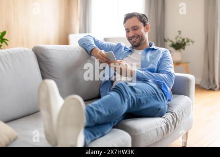 Happy Man Reclining on Couch Using Phone Stock Photo
