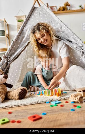 A curly-haired mother and her toddler daughter are happily playing inside a play tent using the Montessori method. Stock Photo