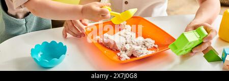Toddler girl exploring and playing with a plastic container of food in a Montessori-inspired learning environment at home. Stock Photo