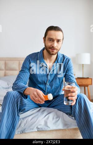 Handsome man sitting on bed, peacefully holding glass of water and pills. Stock Photo