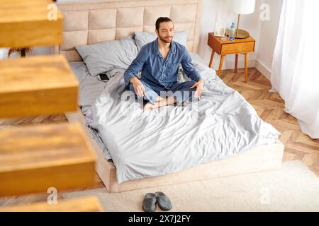 Handsome man peacefully practices morning yoga on his bed. Stock Photo