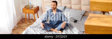 Handsome man peacefully practicing yoga on top of a cozy bedroom bed. Stock Photo