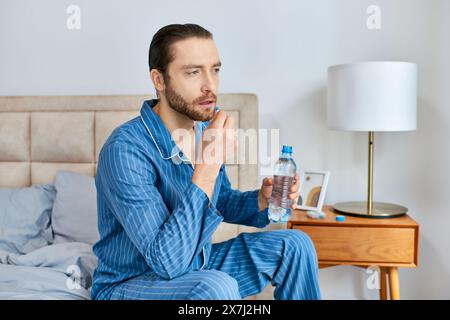 Man sitting on bed, holding water bottle and pill, deep in thought. Stock Photo