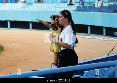 Cuban girl excited to see an image of her dad on the jumbotron at a baseball game in Havana, Cuba and points to it as her mother holds her and looks. Stock Photo