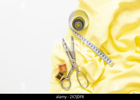 Spools of thread, measuring tape, sewing scissors and yellow fabric on a white background, sewing Stock Photo