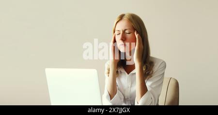 Tired overworked woman employee suffering from headache, migraine, working with laptop sitting at desk in office in morning Stock Photo