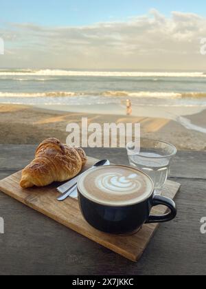 Cup of coffee with croissant on the table in beach cafe at sunny morning closeup Stock Photo