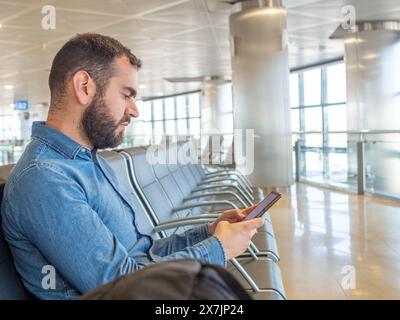 Bearded man using his smarphone while waiting in the airport terminal Stock Photo