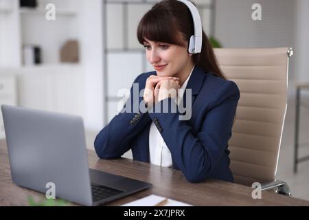 Woman in headphones watching webinar at wooden table in office Stock Photo