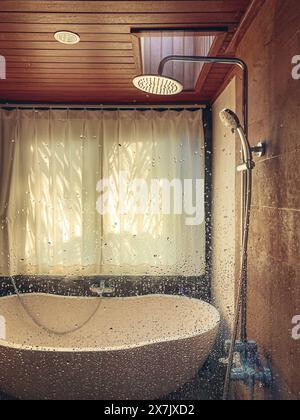 Shower and stone bathtub in bathroom with window and water drops on glass Stock Photo