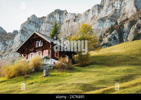 A traditional Swiss chalet nestled on a grassy hill in front of the Churfirsten mountain range, Switzerland, on a calm autumn day Stock Photo
