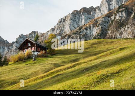 A traditional Swiss chalet nestled on a grassy hill in front of the Churfirsten mountain range, Switzerland, on a calm autumn day Stock Photo