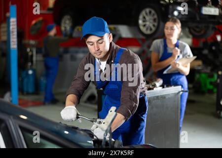 Professional mechanic man in uniform repairing car in auto repair garage Stock Photo