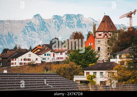 The stone tower of the Red House stands tall in Vaduz, Liechtenstein, nestled among colorful autumn trees and surrounded by mountains Stock Photo