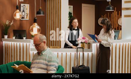 Old person filling in registration forms at front desk, passing check in process and preparing to start retirement holiday trip. Woman with luggage asking receptionist about all inclusive offers. Stock Photo
