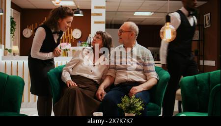 Old people napping on each other in hotel lounge area, waiting to see accommodation and start trip. Retired couple with jetlag after international flight, feeling exhausted on couch. Stock Photo