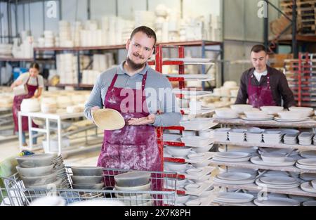 Successful potter displaying handcrafted plate in artisanal pottery studio Stock Photo