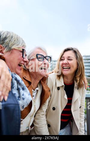 Group of three mature caucasian women enjoying embracing walk together laughing outdoor Stock Photo