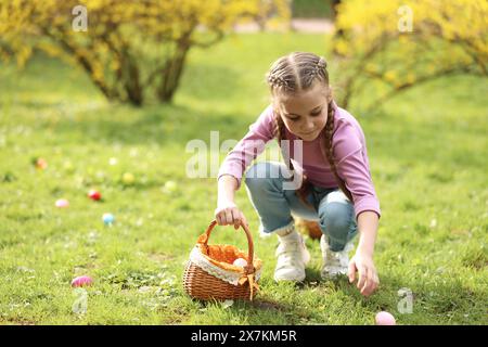 Easter celebration. Cute little girl hunting eggs outdoors, space for text Stock Photo