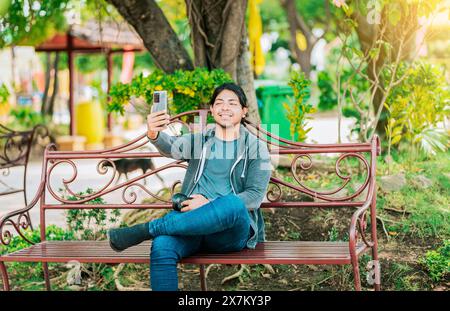 Relaxed guy taking a selfie sitting on a bench at sunset. Smiling man sitting on a bench taking a selfie in Nagarote Park Stock Photo
