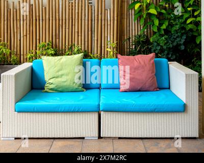 Empty white modern rattan couch seat with blue cushion, sofa with pillows for guests on bamboo wall background at the outdoor garden with nobody. Asia Stock Photo