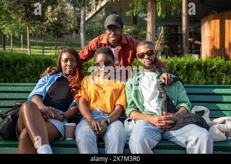 Group of happy african american students sits on bench in university campus looks at camera together Stock Photo