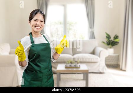 Asian housekeeper wear yellow rubber gloves and green apron smiling and thumb up Stock Photo