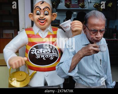 A man having a cup of tea at a branch of Yewale Amruttulya chain of tea shops, with their trademark figure of an old-style Indian tea vendor; Mumbai, Stock Photo