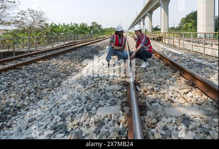 Rail transportation engineer in safety vest and hardhat check the neatness of the railway track while holding walkie-talkie and tablet computer. Stock Photo
