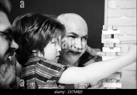 Grandfather watching son and grandson playing board game at home. Happy generational muti three generation men family portrait. Stock Photo
