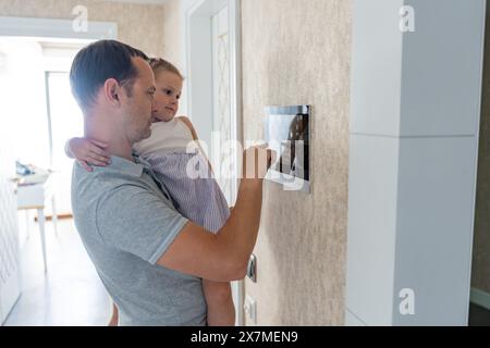 Daughter in her father using tablet panel application for control smart home living. Wireless device controller for home automation IoT on the wall Stock Photo