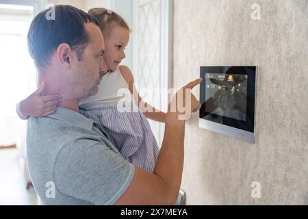 Daughter in her father using tablet panel application for control smart home living. Wireless device controller for home automation IoT on the wall Stock Photo