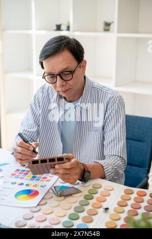 A professional, experienced senior Asian male interior designer or architect focusing on working on a new project in the office, checking material sam Stock Photo