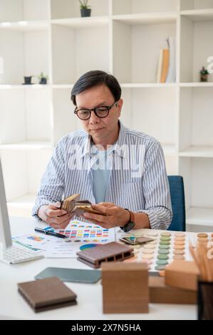A professional, experienced senior Asian male interior designer or architect focusing on working on a new project in the office, checking color sample Stock Photo
