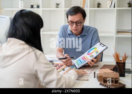 An expert senior Asian male contractor or interior designer is having a meeting with his client to discuss the building interior design, looking at an Stock Photo