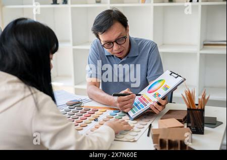 An expert senior Asian male contractor or interior designer is having a meeting with his client to discuss the building interior design, looking at an Stock Photo