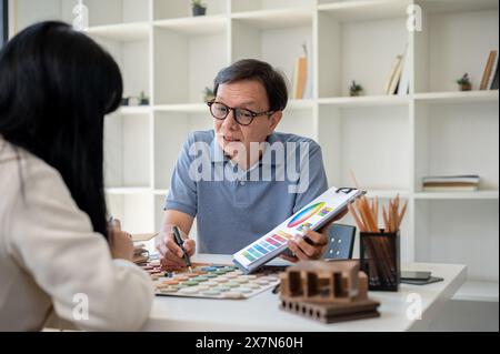 An expert senior Asian male contractor or interior designer is having a meeting with his client to discuss the building interior design, looking at an Stock Photo