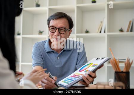 An expert senior Asian male contractor or interior designer is having a meeting with his client to discuss the building interior design, looking at an Stock Photo
