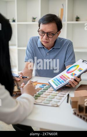 An expert senior Asian male contractor or interior designer is having a meeting with his client to discuss the building interior design, looking at an Stock Photo