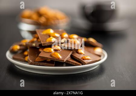 Broken chocolate bar with almonds on plate on a black table. Stock Photo